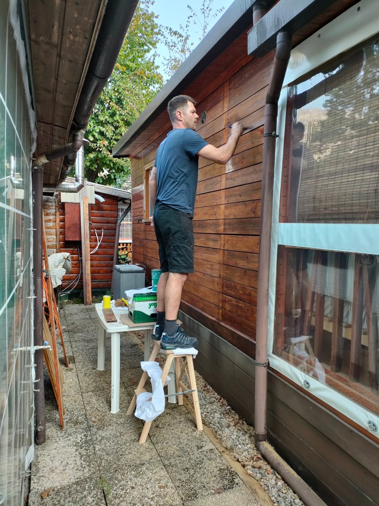 Marcel is de zijkant van het vakantiehuisje aan het beitsen